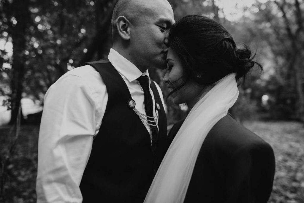 Black & White image of a closeup of Groom kissing Bride on the forehead. Photo taken by Tracey Allsopp Photography 