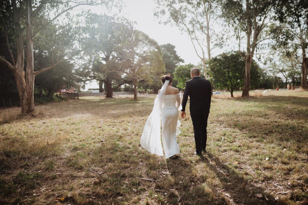Bride & Groom holding hands walking off into the long grass. Photo taken by Tracey Allsopp Photography 